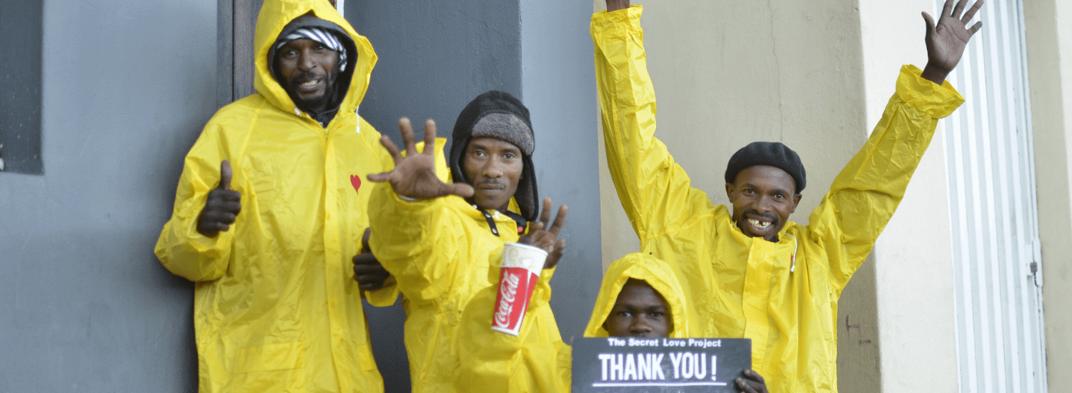 A group of men receiving Rain Suits from The Secret Love Project Homeless Rain Suit Campaign